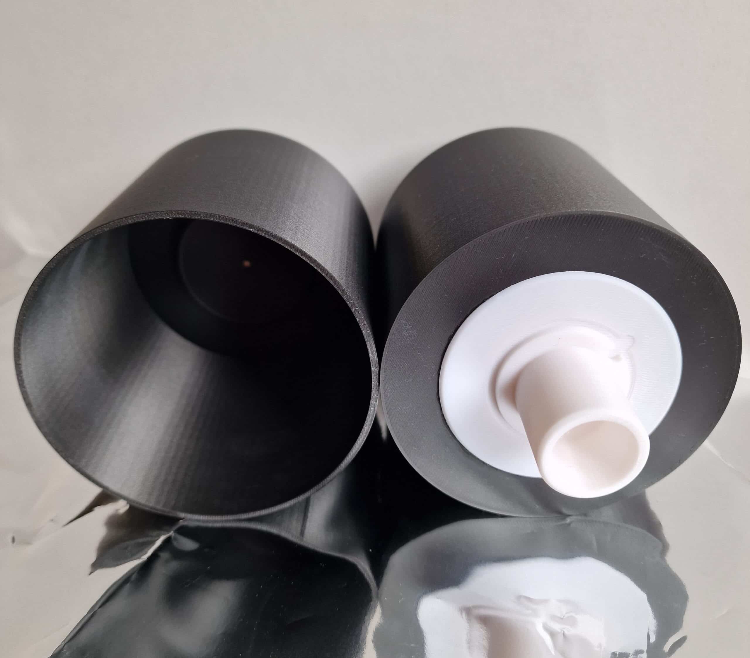 Studio-Foto zweier zylindrischer schwarzer Bauteile mit weißem Adapter